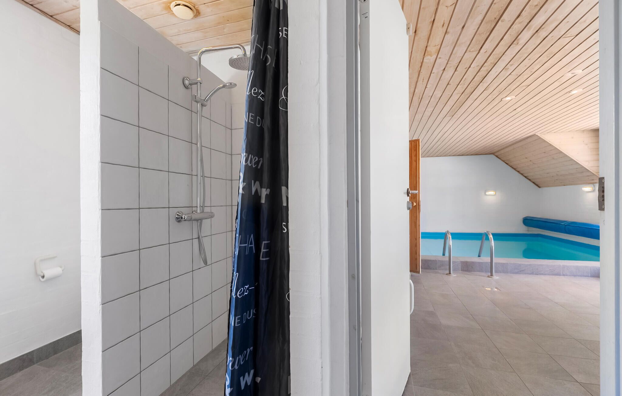 Un baño moderno con ducha, inodoro y vistas a una zona de piscina con una piscina azul y una escalera.