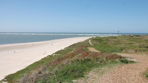 Ein Strand mit blauem Himmel, sandigem Ufer und einem Weg zum Wasser.