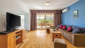 A living room with a TV, wooden furniture, a sofa with cushions, and a view through a glass door to an outdoor area. - Lovely home in Golubovo (Golubovo)