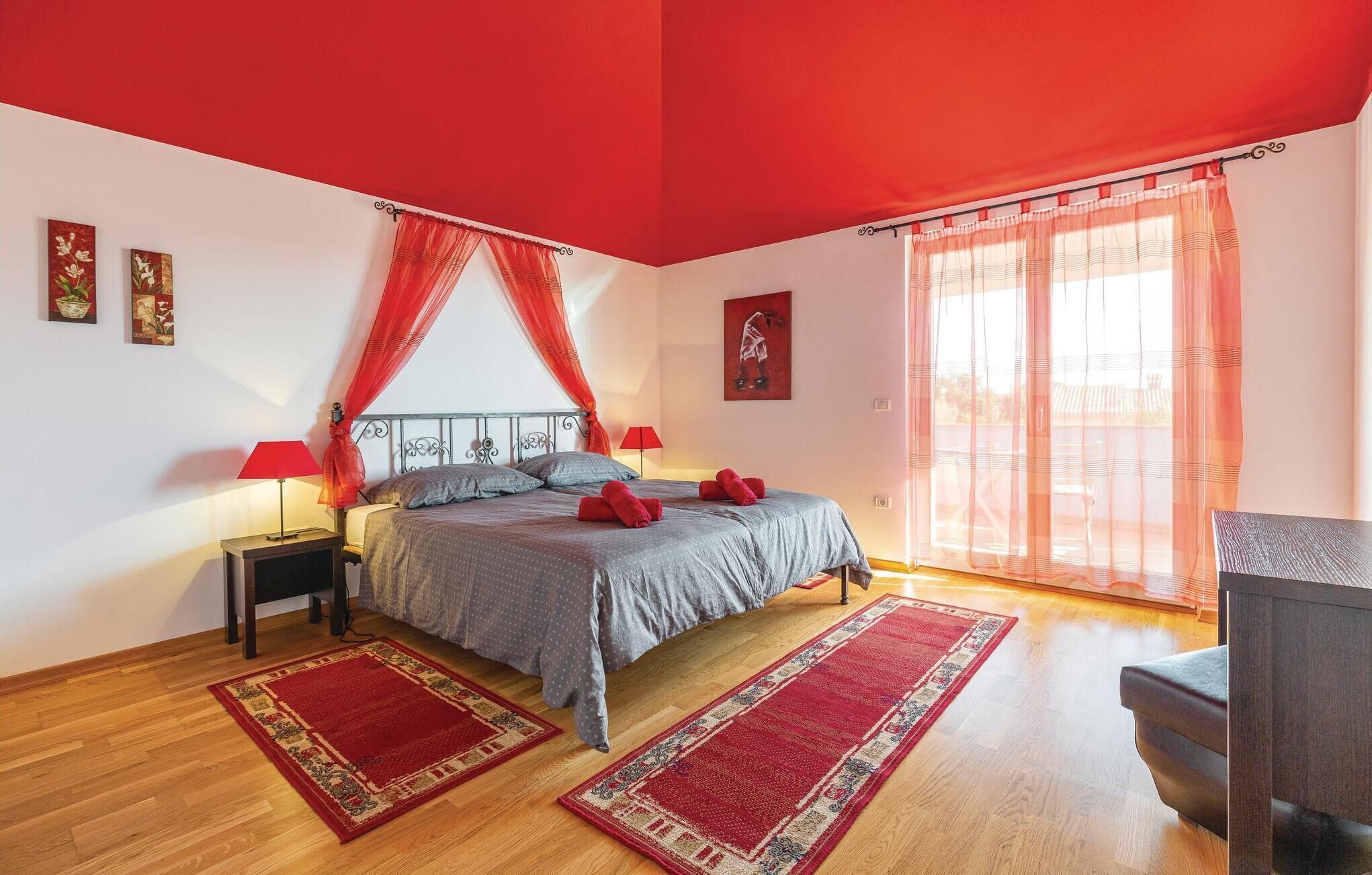 A bedroom with a bed, nightstands, a chair, and a window with sheer curtains.