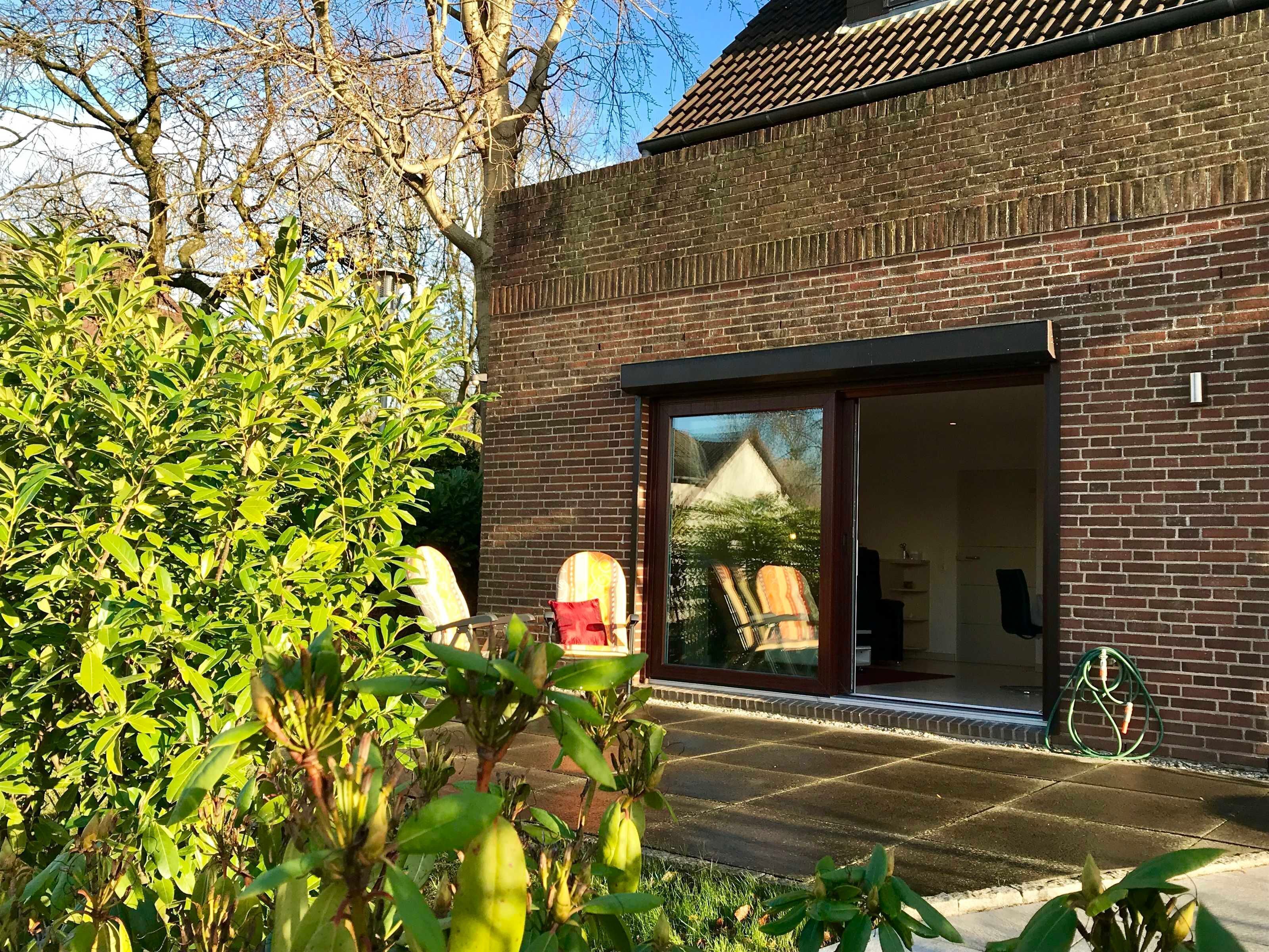 Ein modernes Backsteingebäude mit einer großen Glasdoor und einem kleinen Gartenbereich mit Grünpflanzen.