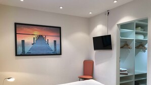 Un dormitorio con cama, televisor, armario y un cuadro de un muelle.