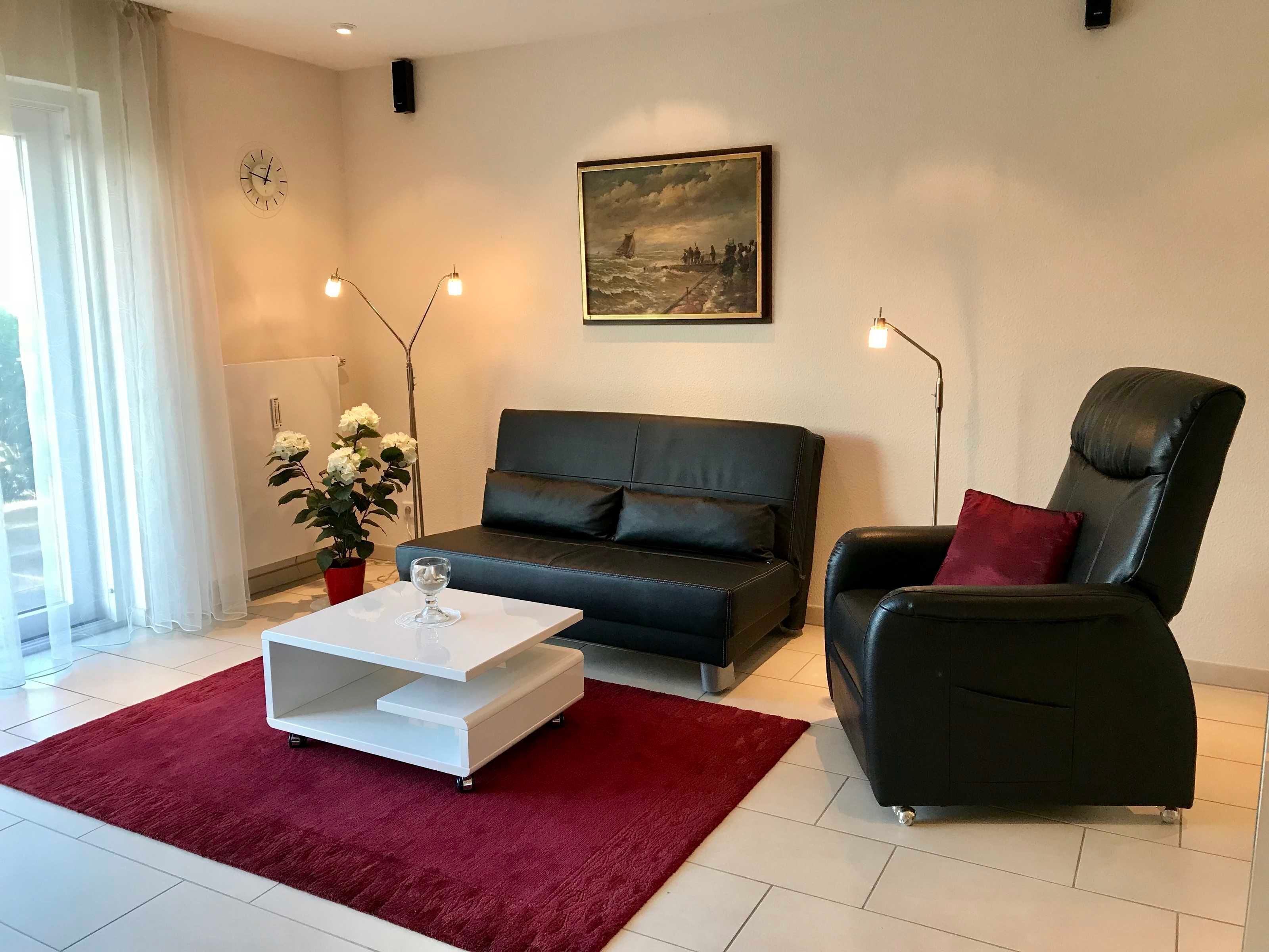Ein modernes Wohnzimmer mit einem schwarzen Ledersofa, einem roten Teppich, einem weißen Couchtisch und einem Gemälde an der Wand.