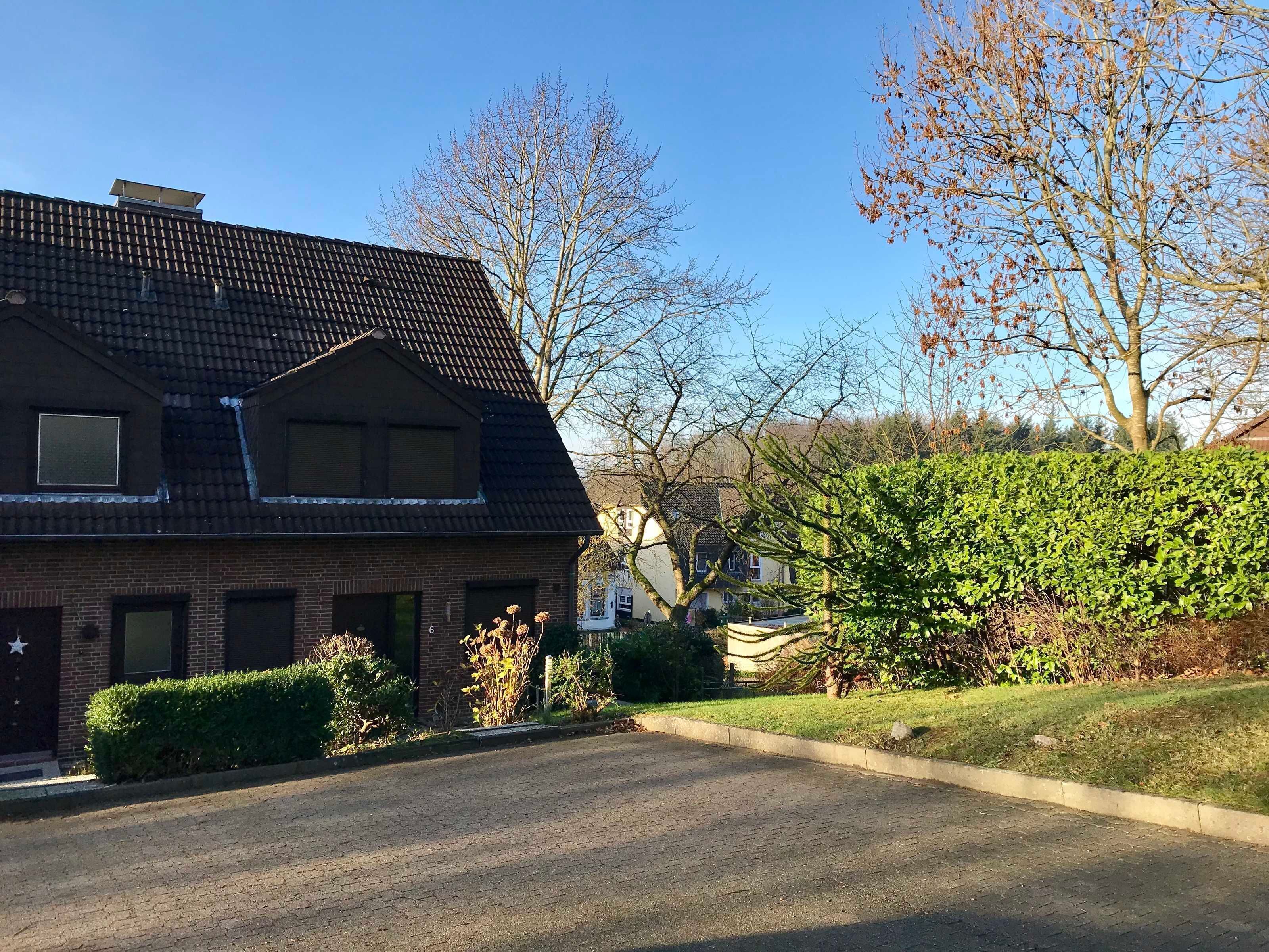 Ett bostadshus med ett sluttande tak, en fasad av tegel och en liten trädgård framför huset, avgränsad av en häck.