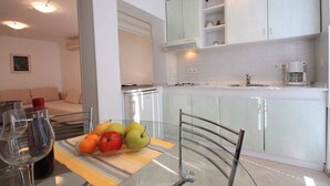 A modern kitchen with white cabinets, a glass table with fruit, and a coffee maker. - Holiday apartment with terrace near the beach (Crikvenica)
