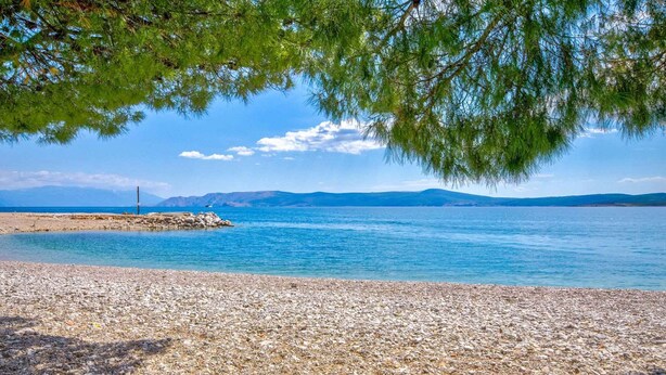 A pebbled beach with clear blue water and distant mountains. - Holiday apartment with terrace near the beach (Crikvenica)