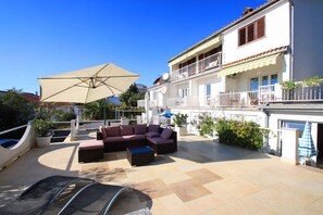 A rooftop patio with outdoor furniture, a large umbrella, and a white building with balconies.