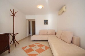 A living room with a beige sofa, a wooden coat rack, a patterned rug, and a wall-mounted air conditioner.