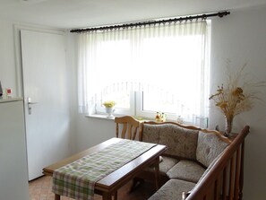 A dining area with a wooden table and bench, a window with curtains, and a vase with dried flowers on the windowsill. - Apartment 36 - Apartments on Usedom (Rankwitz)