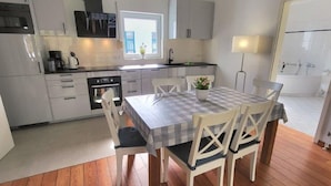 Una cocina moderna con armarios blancos, una mesa de comedor con mantel a cuadros y suelo de madera.