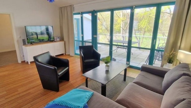 Una sala de estar con un sofá, dos sillones, un televisor y una mesa con una planta.