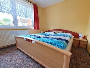 Una camera da letto con un letto, un comodino, una lampada, una finestra con tende e un termosifone.