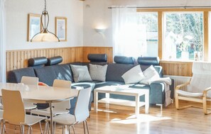 A modern living room with a sectional sofa, a round dining table with chairs, and a large window offering a view of trees. - 3 bedroom stunning home in Yngsjö (Yngsjö)