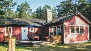 Ett rött trähus med en veranda, en skorsten och en liten uteplats.