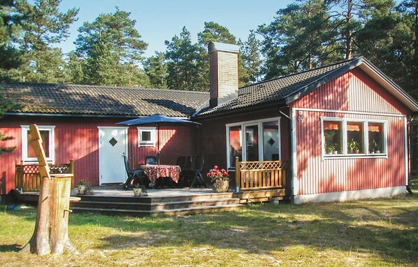 A red wooden house with a porch, a chimney, and a small deck area.