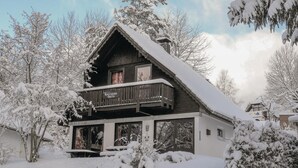 Een houten chalet met een balkon, omringd door met sneeuw bedekte bomen.