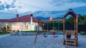 A wooden swing set in a gravel area with a house in the background.
