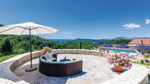 A circular outdoor seating area with a pool, surrounded by stone flooring and potted flowers.