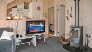 A cozy living room with a television, a sofa, a coffee table, a fireplace, and wooden walls. - Gorgeous home in Oksbøl with sauna (Oksbøl)