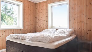 Ein Schlafzimmer mit einem Bett, Holzwänden und zwei Fenstern.
