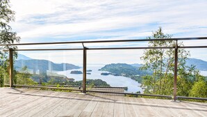 Eine Holzdar Terrasse mit Glasgeländer mit Blick auf einen See und Berge.