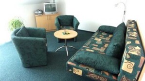 Une petite pièce agréable et chaleureuse, avec un canapé vert, deux fauteuils, une petite table ronde et un téléviseur posé sur un meuble en bois.