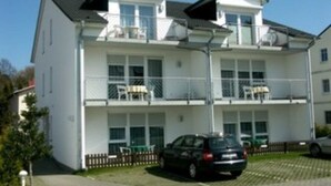 Un immeuble de deux étages doté de balcons, une voiture garée devant, et un ciel dégagé.