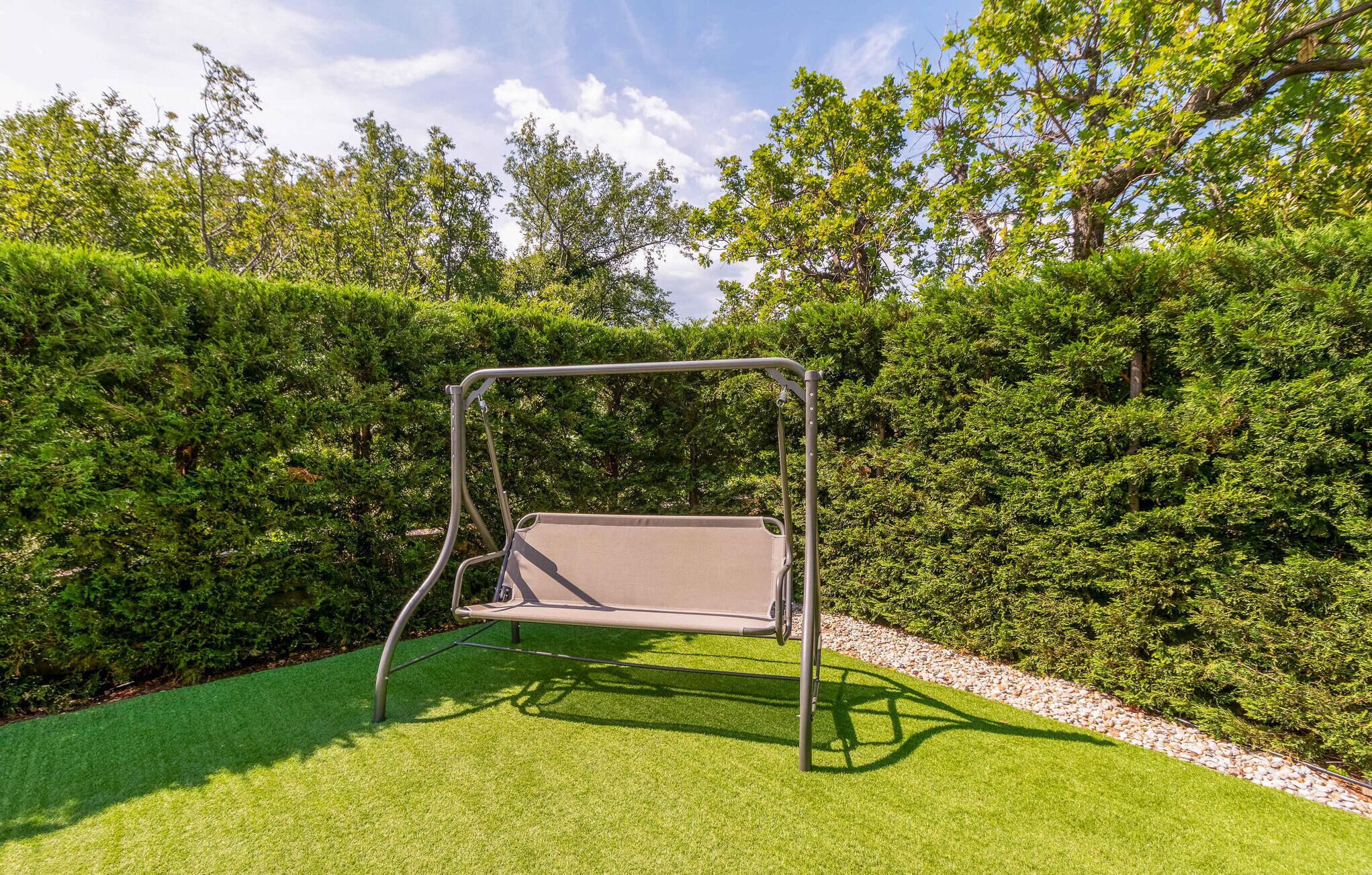 A swing set in a well-maintained garden with green grass and dense hedges.