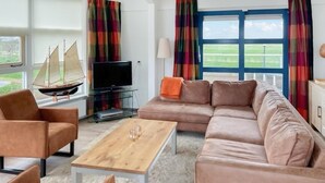 A living room with a sofa, armchairs, a coffee table, a television, and a sailboat model.