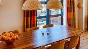 A dining area with a wooden table, two hanging wicker lamps, and a bowl of oranges.