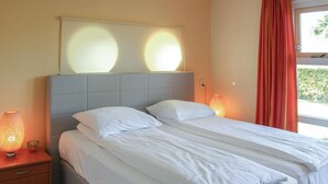 A neatly made bed with white linens, a grey headboard, and two bedside lamps.
