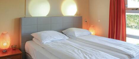 A neatly made bed with white linens, a grey headboard, and two bedside lamps.