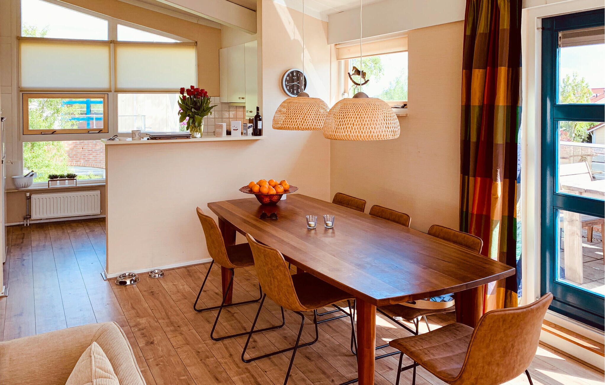 A dining area with a wooden table, chairs, a bowl of oranges, and a vase of flowers.