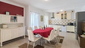 A modern kitchen with white cabinets, a dining area with a red tablecloth, and a red wall with a clock.