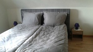 A bed with a grey headboard and two pillows, flanked by two nightstands with lamps.