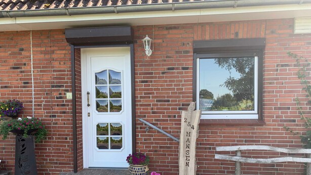 A brick building with a white door, a window, and a wooden sign with the name 'Hans'.