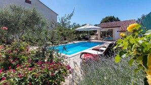 A swimming pool surrounded by lush greenery and flowers, with a building in the background. - Amazing apartment in Pula (Pula)