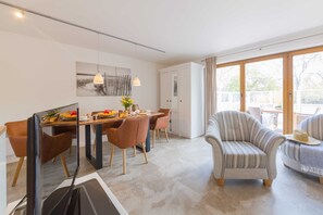 Un espace de salle à manger moderne, avec une table en bois, des chaises marron et une grande fenêtre agrémentée de rideaux.