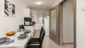 A modern kitchen with white cabinets, a dining table set with plates and glasses, and a microwave. - Beach front apartment in Crikvenica (Crikvenica)