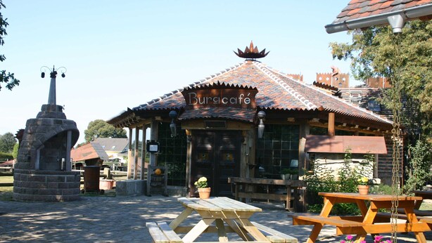 Un bâtiment rustique appelé « Buracafe », doté d’un toit en tuiles et situé à proximité d’un monument en pierre.