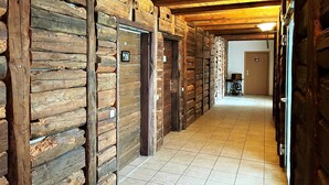 Un couloir aux murs en bois et au sol carrelé, qui mène à une pièce dotée d’une porte et d’une petite table.