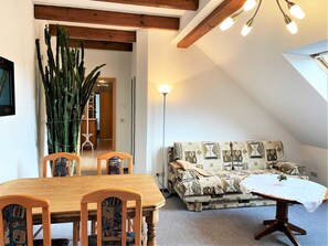 A cozy room with a wooden dining table and chairs, a patterned sofa, and a large cactus plant.