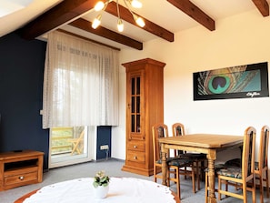 A dining area with a wooden table and chairs, a cabinet, and a window with curtains.