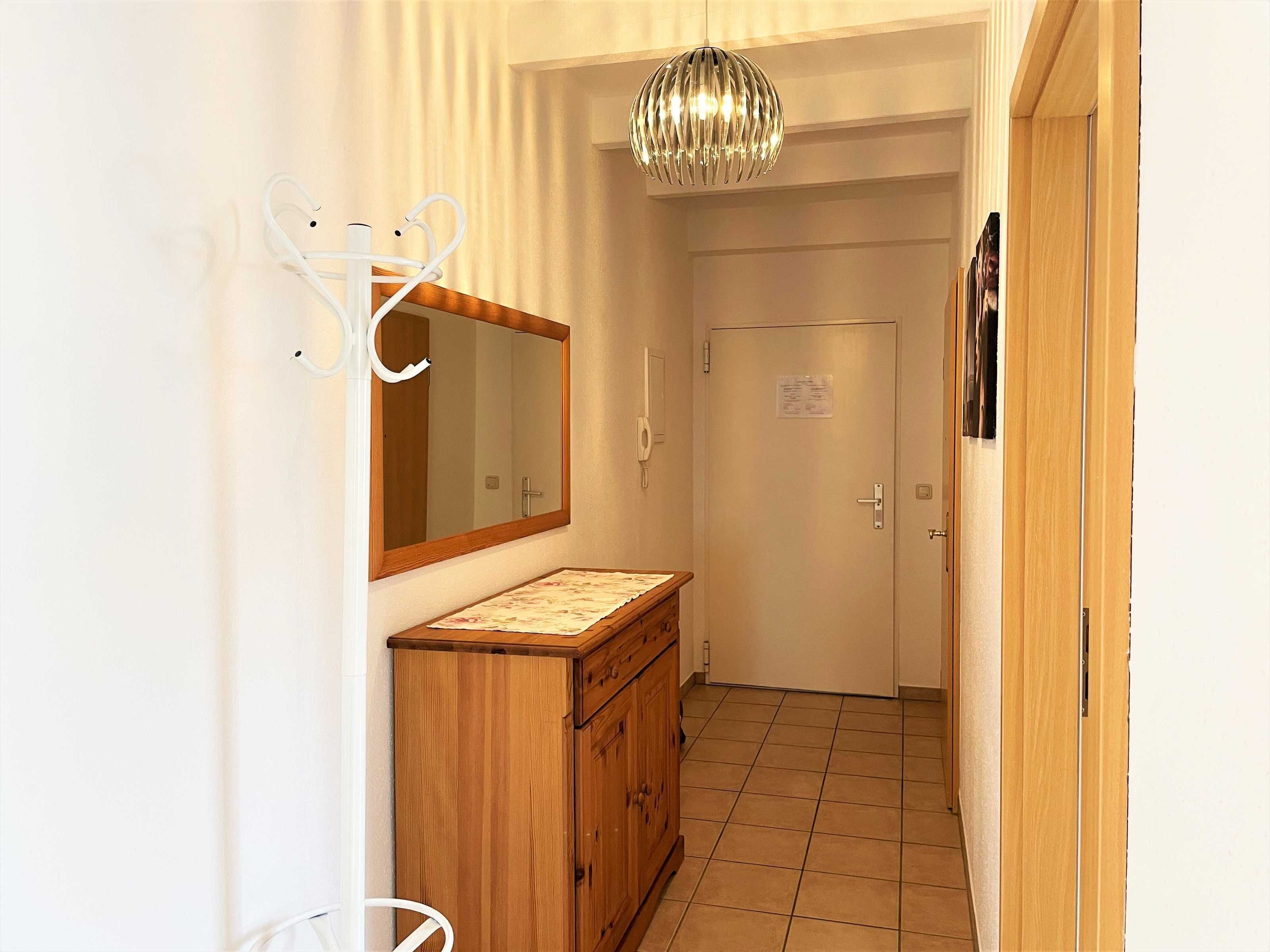 A hallway with a wooden cabinet, a mirror, a door, and a hanging light fixture.