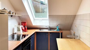 Une cuisine compacte dotée d’un puits de lumière, d’une cafetière rouge, d’un évier et d’une petite fenêtre.