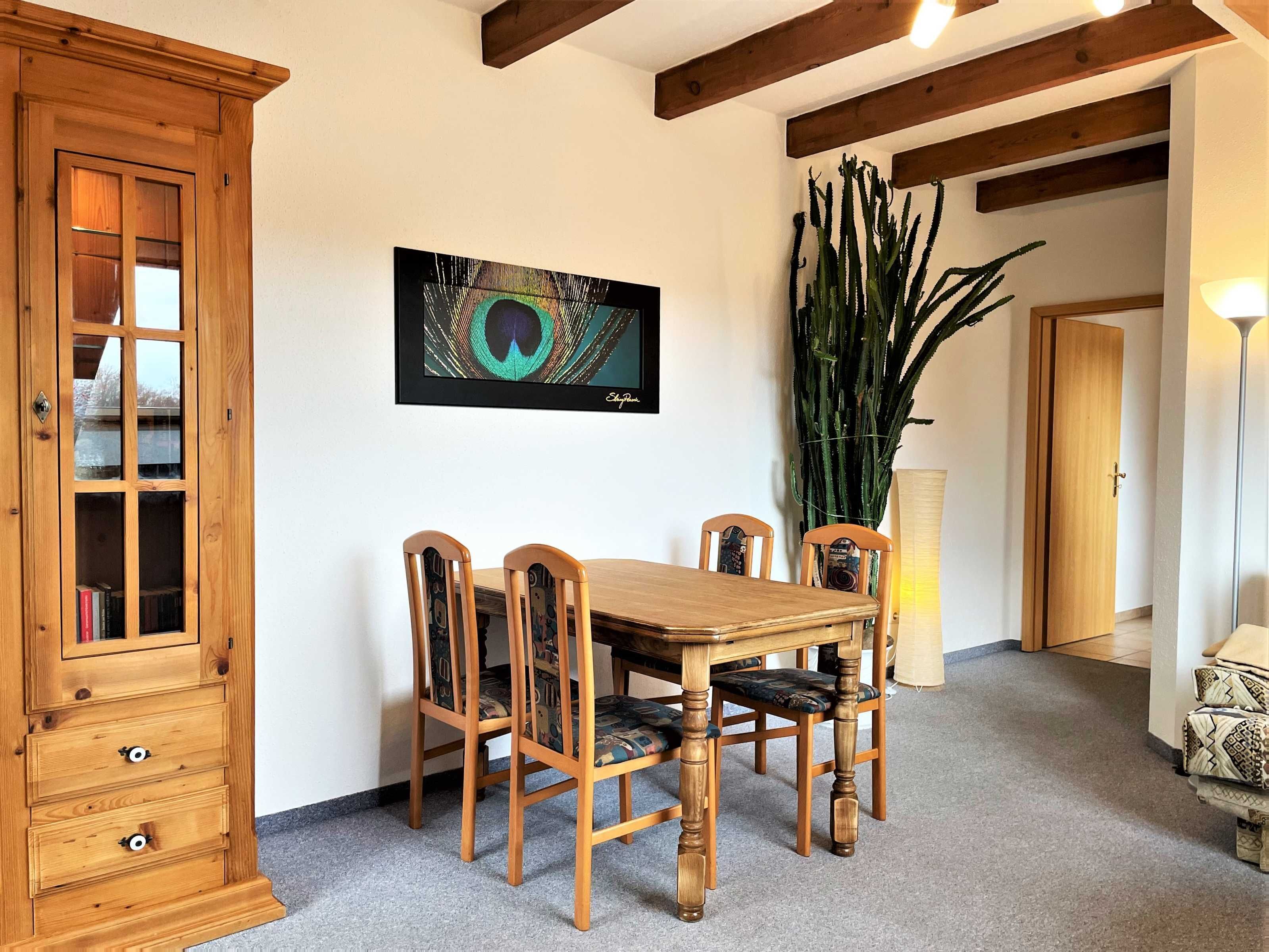 Un comedor con una mesa y sillas de madera, un aparador de madera, una obra de arte enmarcada y una planta alta.
