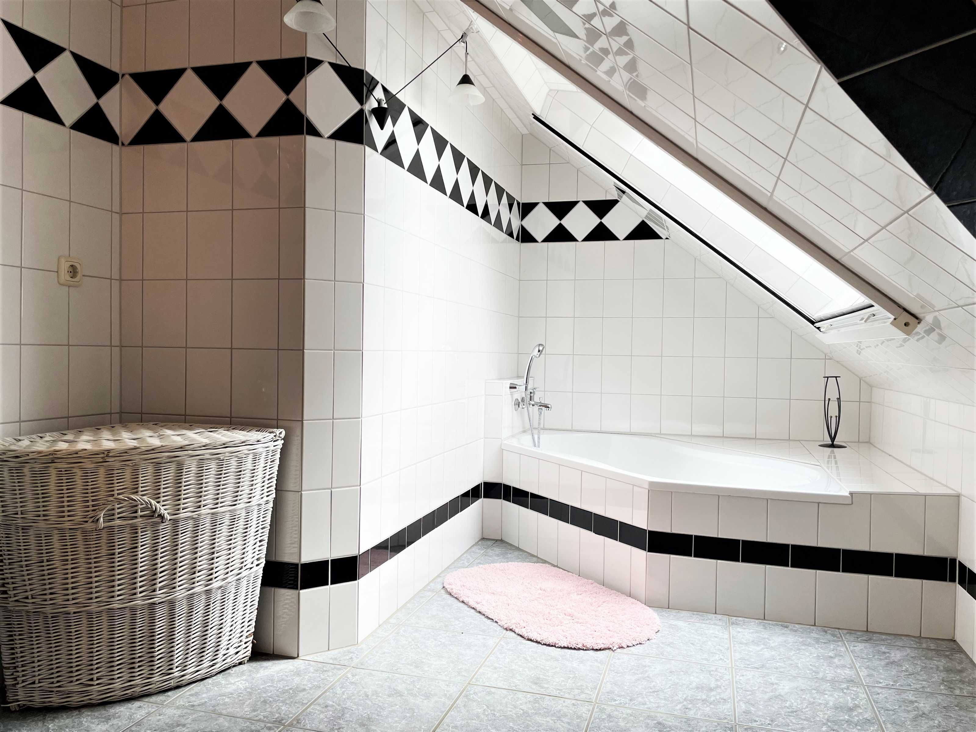 A modern bathroom with a freestanding bathtub, a wicker basket, and a pink rug.