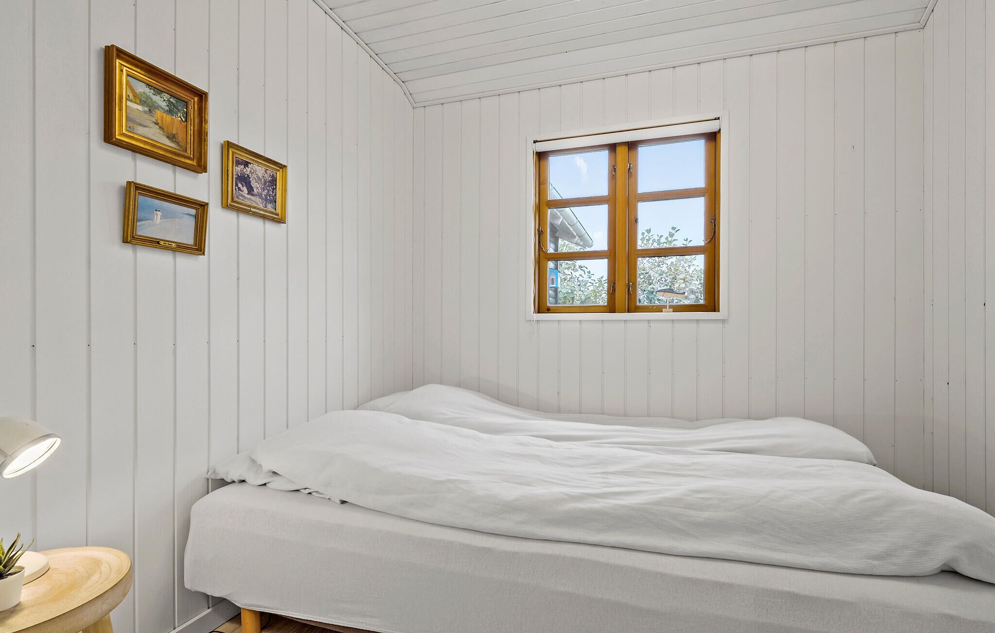 Ein Schlafzimmer mit einem Bett, einem Fenster und drei gerahmten Bildern an der Wand.