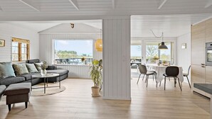 Ein großzügiger Wohnbereich mit Sofa, Couchtisch und Esstisch. Ein großes Fenster bietet einen Blick ins Freie.