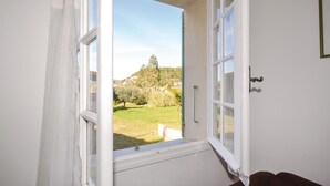 Ventana abierta con vistas a un área verde y árboles.